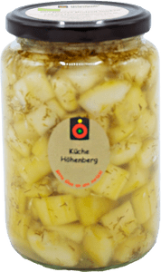 KI generiert: Das Bild zeigt ein Glas mit eingelegten Weißkäsequadraten, das mit Olivenöl und Kräutern gefüllt ist. Auf dem Glasdeckel und seitlich befindet sich ein Etikett mit der Aufschrift "Küche Höthenberg".