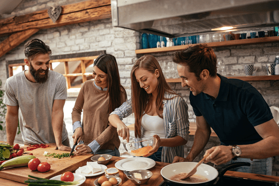 KI generiert: Vier Personen kochen gemeinsam in einer modernen, gemütlichen Küche und schneiden Gemüse oder rühren Zutaten. Die Atmosphäre wirkt fröhlich und entspannt.
