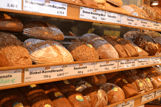 KI generiert: Das Bild zeigt eine Bäckereiauslage mit verschiedenen Brotsorten, die deutlich ausgezeichnet sind. Die Produkte sind mit Preisschildern versehen, die die jeweiligen Brotsorten und Preise angeben.