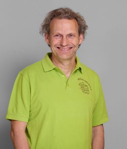 KI generiert: Ein Mann in einem grünen Poloshirt lächelt in die Kamera vor einem grauen Hintergrund.