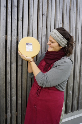 KI generiert: Eine Person hält einen runden Laib Käse vor einer Holzwand.