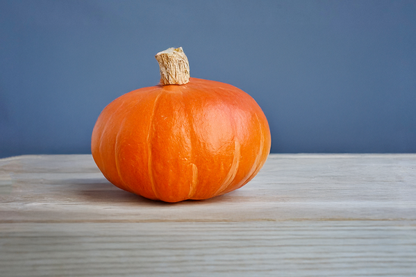 KI generiert: Ein einzelner Kürbis auf einem Holztisch vor einem blauen Hintergrund.