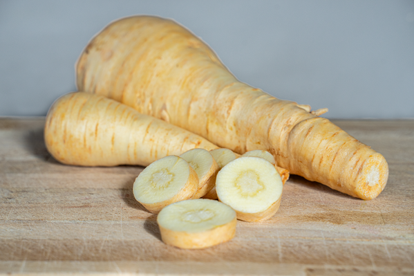 KI generiert: Das Bild zeigt frische Pastinaken, die auf einem Stück Jute liegen. Um die Pastinaken herum liegen grüne Blätter.