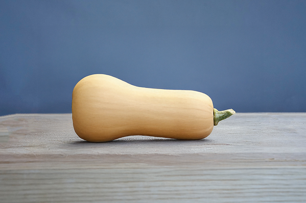 KI generiert: Ein Butternut-Kürbis liegt auf einem Holztisch vor blauem Hintergrund.