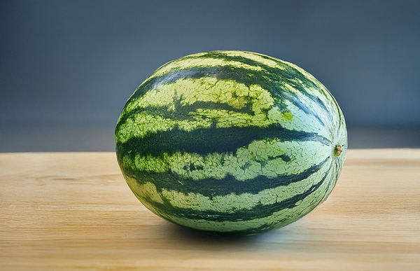 KI generiert: Eine Wassermelone liegt auf einem Holztisch vor neutralem Hintergrund.
