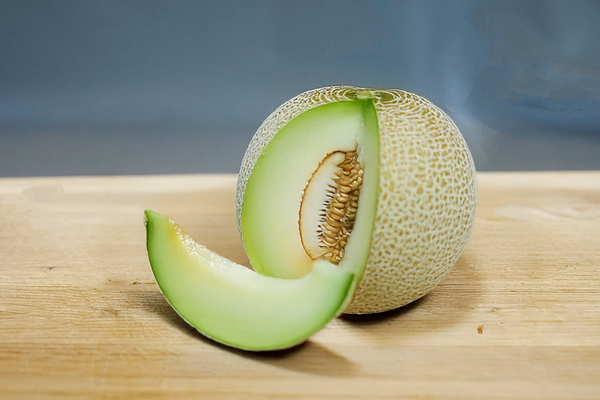 KI generiert: Eine aufgeschnittene Honigmelone mit einem einzelnen Melonenstück davor auf einem Holzbrett.