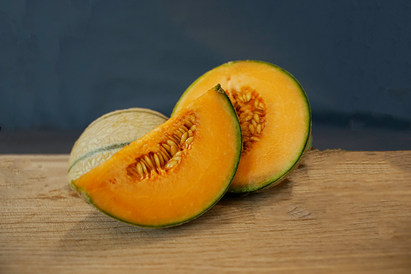 KI generiert: Aufgeschnittene Melone auf Holztisch, orangefarbenes Fruchtfleisch und Kerne sichtbar.