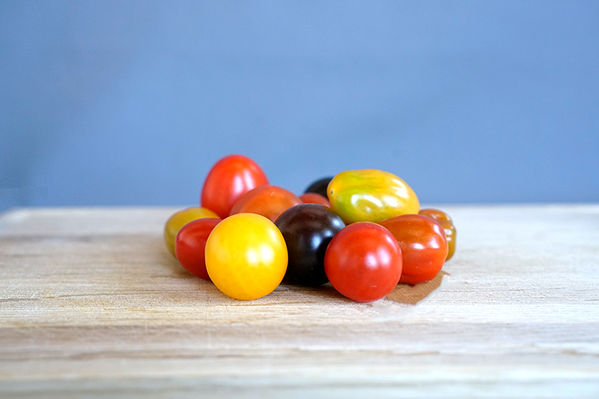 KI generiert: Mehrfarbige Kirschtomaten auf einem Holzbrett vor blauem Hintergrund.