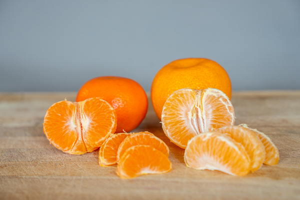 KI generiert: Ganze und geschälte Mandarinen sowie Mandarinenspalten auf einem Holzbrett.