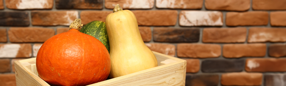 KI generiert: Drei Kürbisse in einer Holzkiste vor einer Ziegelwand.