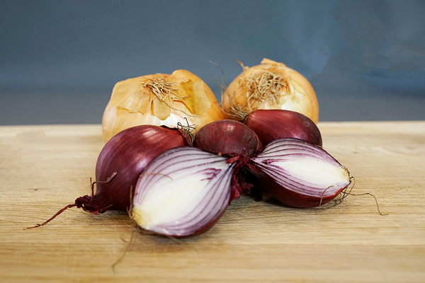 KI generiert: Rote und gelbe Zwiebeln liegen auf einem Holztisch, eine rote Zwiebel ist halbiert.