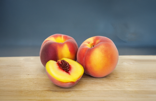 KI generiert: Drei Pfirsiche auf Holzuntergrund, einer ist halbiert und zeigt den Kern.