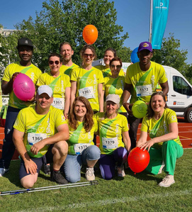 KI generiert: Das Bild zeigt eine Gruppe von Menschen in gelben T-Shirts, die lächeln und auf einem Rasen mit bunten Ballons posieren. Sie tragen Startnummern, was auf die Teilnahme an einem sportlichen Event hindeutet.
