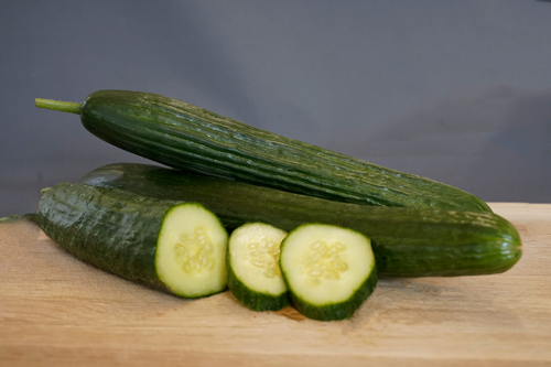 KI generiert: Zwei ganze Gurken und drei Gurkenscheiben auf einem Holzbrett.