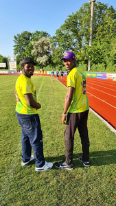 KI generiert: Das Bild zeigt zwei Personen auf einer Laufbahn, die gelbe T-Shirts tragen und in die Kamera lächeln. Im Hintergrund ist eine grüne Wiese und Bäume zu sehen.
