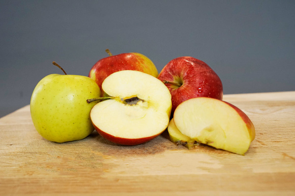 KI generiert: Mehrere Äpfel, darunter geschnittene, auf einem Holztisch vor grauem Hintergrund.