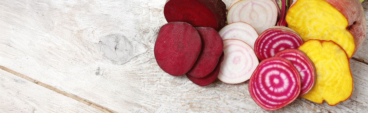 KI generiert: Das Bild zeigt mehrere Pastinaken, frische und in Scheiben geschnittene, auf einer hellen Holzoberfläche. Daneben liegen einige grüne Blätter zur Dekoration.