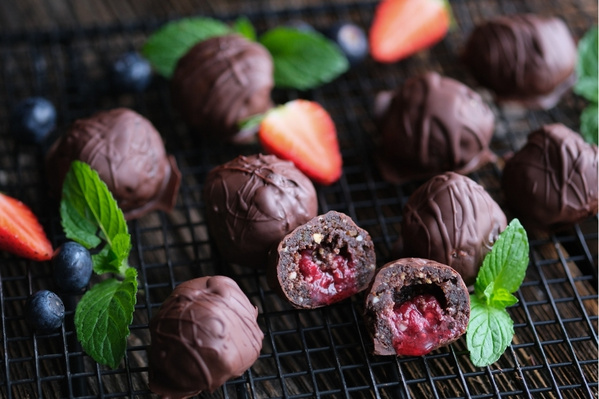 KI generiert: Schokoladentrüffel mit Fruchtfüllung auf einem Gitter, umgeben von Minzblättern und Beeren.