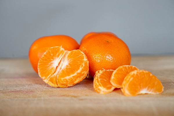 KI generiert: Einige Mandarinen, einige ganz und einige geschält, liegen auf einem Holzbrett.