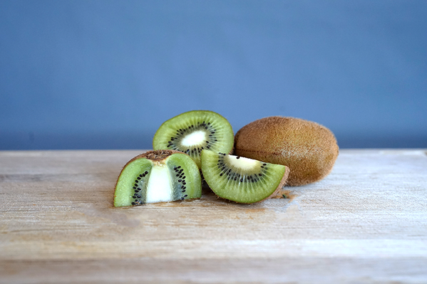 KI generiert: Eine ganze Kiwi und zwei geschnittene Kiwischeiben auf einem Holztisch.
