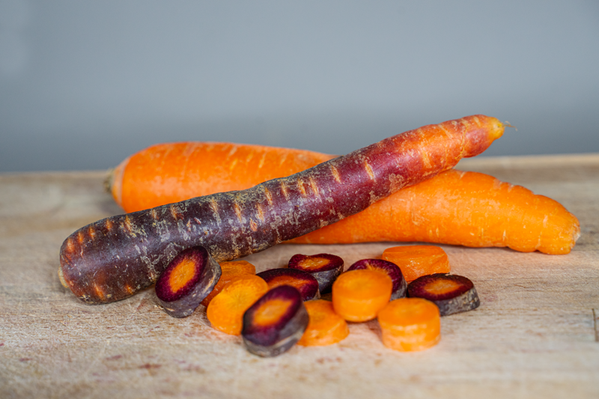 KI generiert: Das Bild zeigt einen Bund frischer Möhren mit grünem Blattwerk, die auf einem hellen Tuch liegen. Die Möhren sind lebendig orange und scheinen frisch geerntet zu sein.
