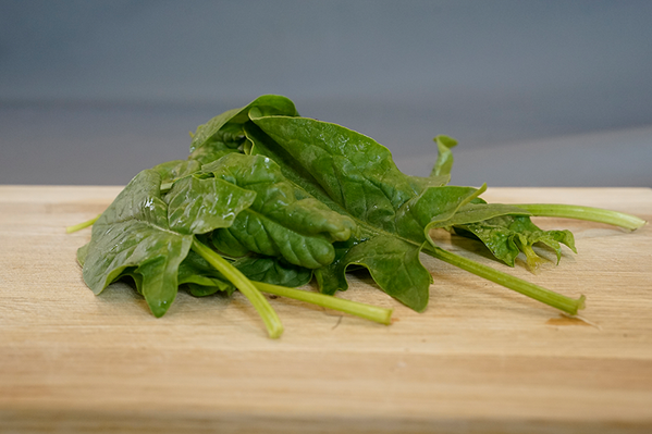 KI generiert: Frischer Spinat auf einem hölzernen Schneidebrett.