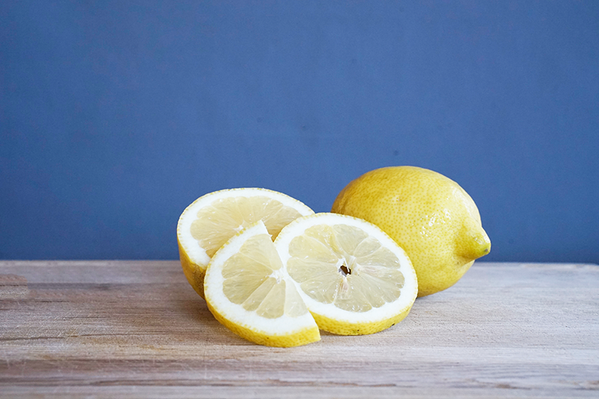 KI generiert: Ganze und geschnittene Zitronen auf einem Holzbrett vor blauem Hintergrund.