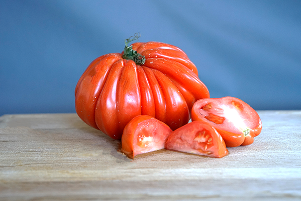 KI generiert: Eine große gerippte Tomate und Tomatenstücke auf einem Holzbrett.
