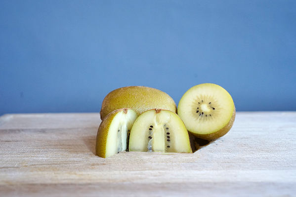 KI generiert: In der Mitte ein aufgeschnittener gelber Kiwi auf einem Holzbrett vor grauem Hintergrund.
