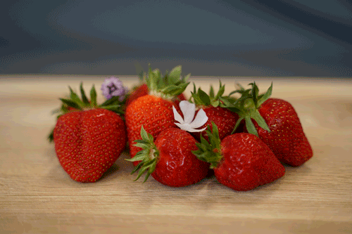 KI generiert: Ein animiertes Bild zeigt frische Erdbeeren mit blühenden Blumen auf einem Holzbrett.