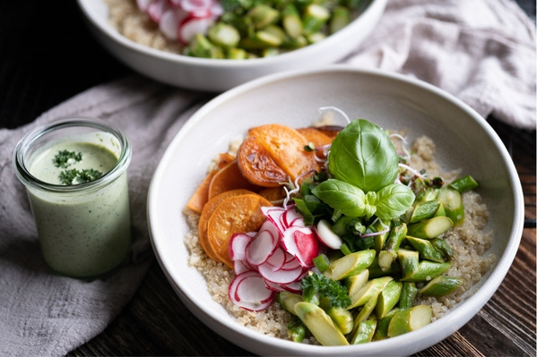 KI generiert: Schale mit bunter Buddha Bowl aus Gemüse und Quinoa, daneben ein Glas grüner Kräutersauce.