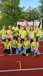 KI generiert: Eine Gruppe von Menschen in grünen T-Shirts feiert freudig auf einem Sportplatz, möglicherweise nach einem Lauf-Event. Sie halten Getränke in den Händen und wirken ausgelassen und glücklich.