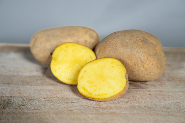 KI generiert: Das Bild zeigt eine Sammlung von Kartoffeln, die in einem Leinenbeutel auf einem Holztisch liegen. Ein Zweig frischer Rosmarin ist neben den Kartoffeln platziert.